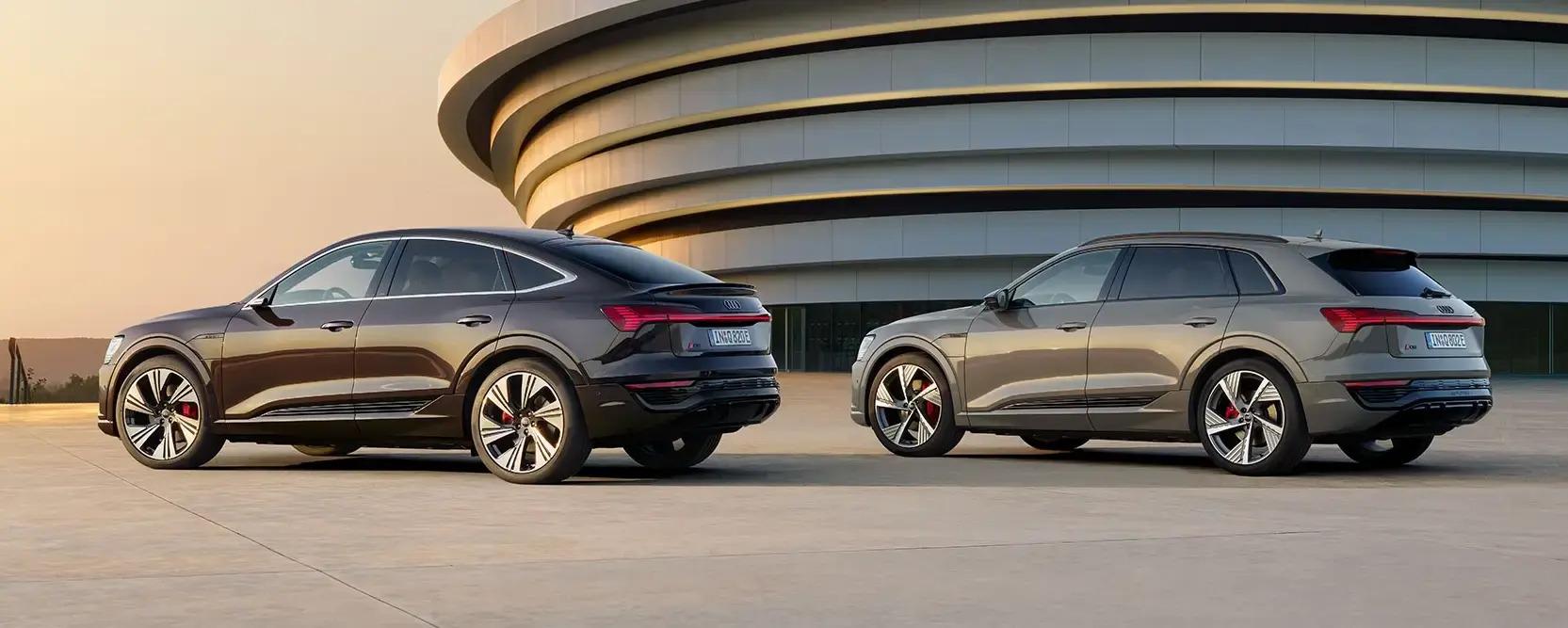 zwei Audi Q8 e-tron Modelle in braun und grau stehen vor einem runden Gebäude im Sonnenuntergang