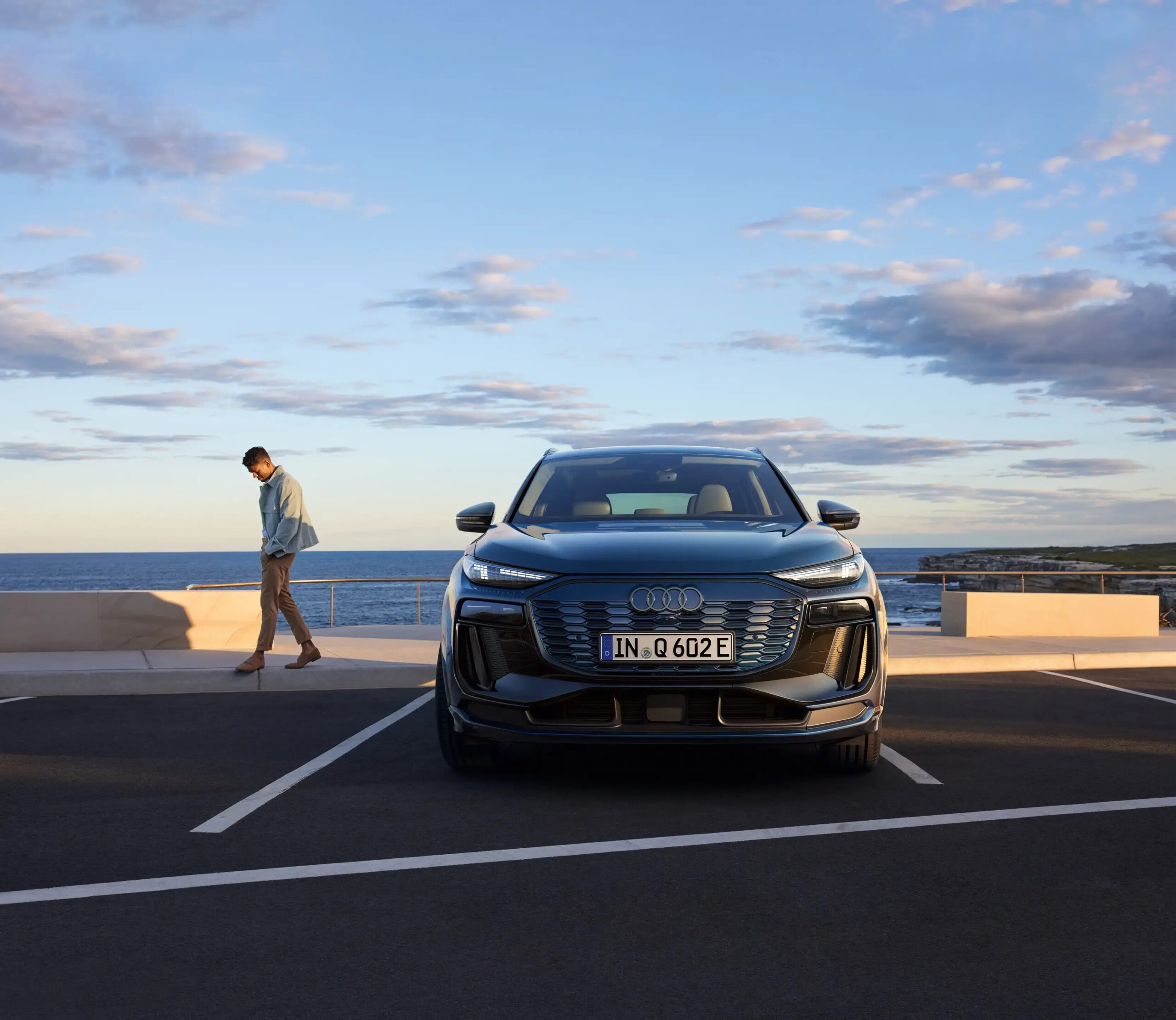 Schwarzer Audi Q6 e-tron Elektroauto frontal geparkt am Meer, Mann geht links vorbei