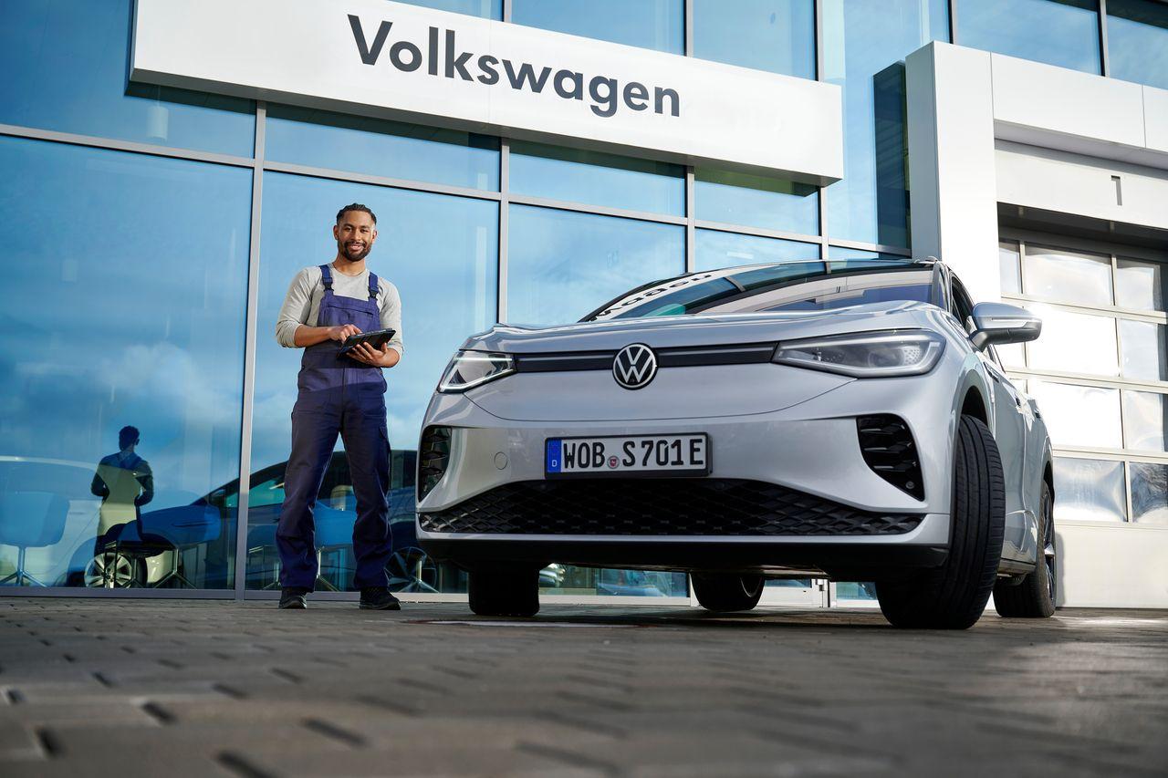 Job & Karriere 4 VW Kfz-Mechatroniker steht mit Diagnosegerät neben einem grauen Volkswagen Elektrofahrzeug