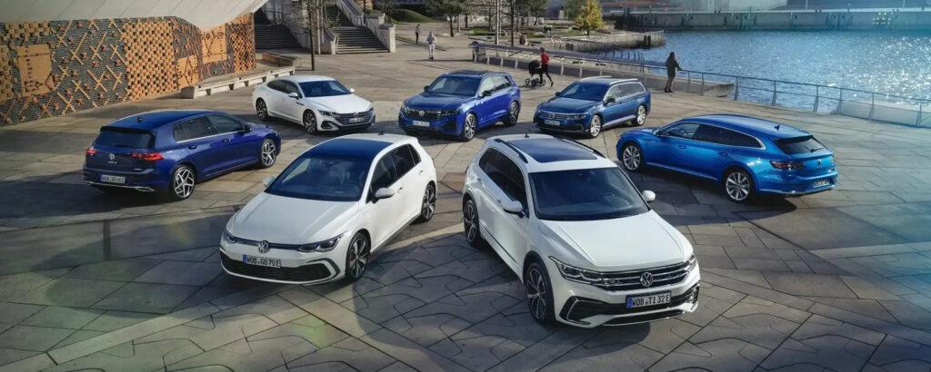 Mehrere VW-Fahrzeuge stehen in einem Halbkreis auf einer gepflasterten Fläche, sofort verfügbar als Lagerwagen.