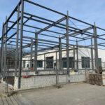 Erweiterung des Werkstattbereichs im Autohaus Hans Maier 4 Stahlgerüst eines Gebäudes im Rohbau vor einer weißen Halle unter blauem Himmel
