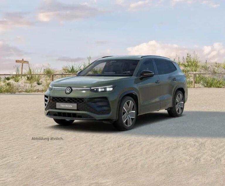 Tayron R-Line eHybrid 5 Volkswagen Tayron SUV in mattem Grün auf sandigem Untergrund vor bewölktem Himmel