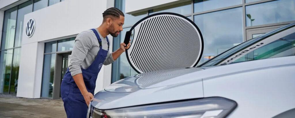 Werkstattmitarbeiter prüft Lackschäden am Volkswagen