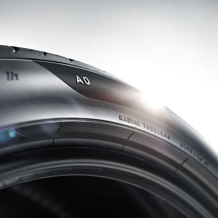 Reifenwechsel-Aktionstage im Herbst 37 Nahaufnahme eines schwarzen Autoreifens mit der Aufschrift 'AO' und 'RADIAL TUBELESS' auf der Seitenwand, Sonnenlicht reflektiert auf der Oberfläche.