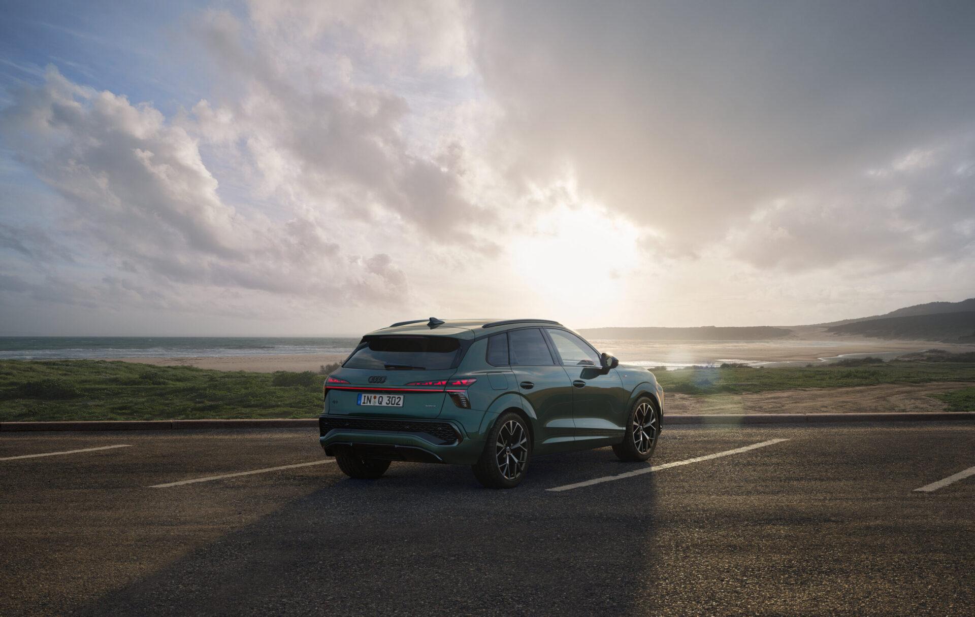Dunkelgrüner Audi Q3 SUV von hinten auf Parkplatz mit Meer und bewölktem Himmel im Hintergrund.