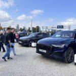 Ein dunkelblauer Audi Q8 und ein schwarzer Audi Q5 auf einem Schotterplatz bei der Automobilausstellung Erding 2025, umgeben von Besuchern und Werbebannern.