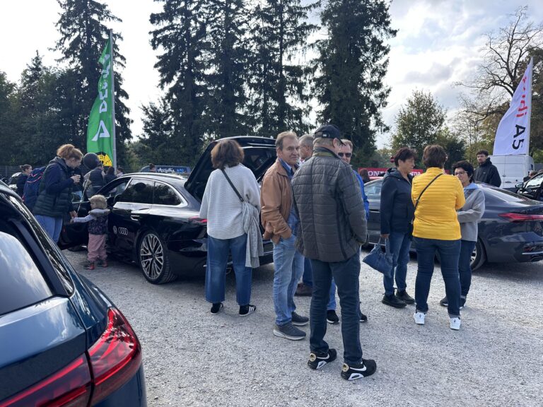 Großes Interesse an der Automobil Ausstellung Erding 2025 22 Mehrere Personen stehen um drei schwarze Audi-Fahrzeuge auf einem Schotterplatz, im Hintergrund Bäume und Fahnen mit den Aufschriften 'Audi A5' und 'Dekra'.