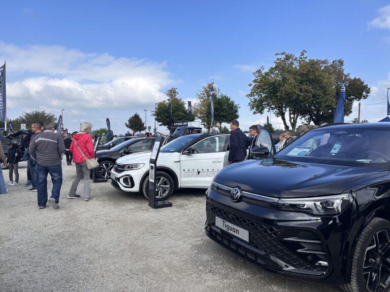 Großes Interesse an der Automobil Ausstellung Erding 2025 23 Außenbereich der Automobilausstellung Erding 2025 mit mehreren geparkten Autos, darunter ein schwarzer Volkswagen Tiguan im Vordergrund, und Besuchern auf Kiesboden unter blauem Himmel mit Wolken.