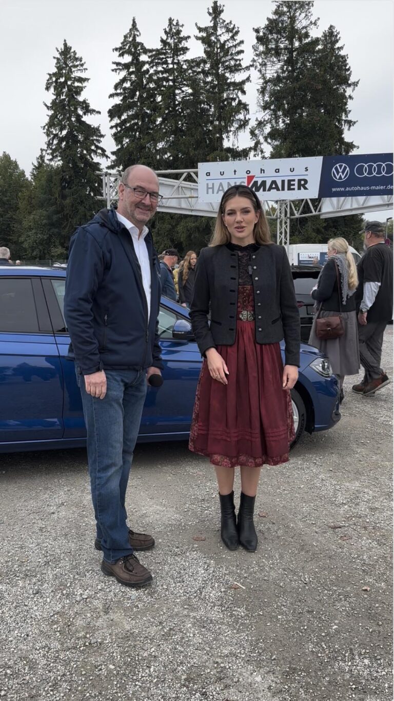 Großes Interesse an der Automobil Ausstellung Erding 2025 16 Zwei Personen stehen vor einem blauen Auto auf einem Schotterplatz, im Hintergrund Bäume und ein Banner mit der Aufschrift 'Autohaus Hans Maier' und Audi-Logo.