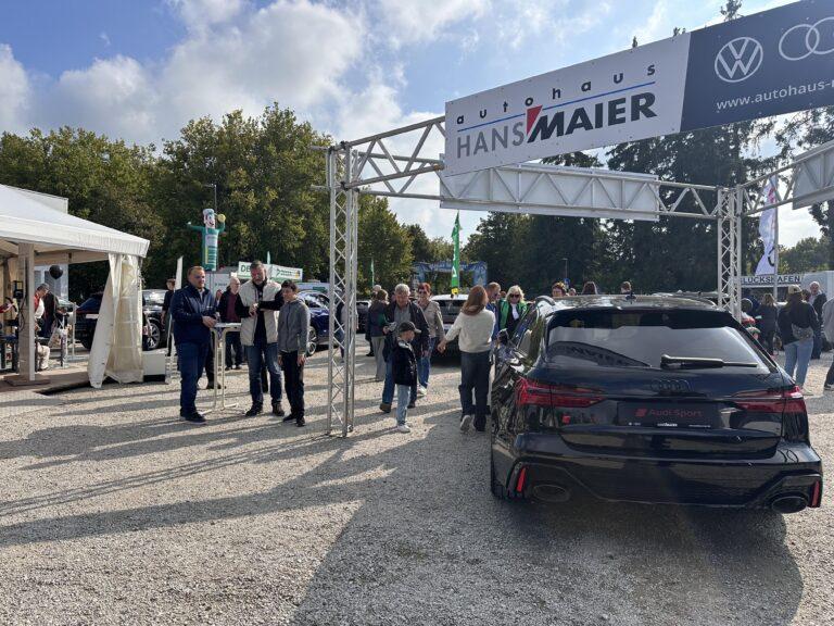 Großes Interesse an der Automobil Ausstellung Erding 2025 6 Schwarzes Audi Sport Auto steht unter einem Metallgestell mit Banner 'Autohaus Hans Maier', umgeben von Menschen auf Automobilausstellung Erding 2025.