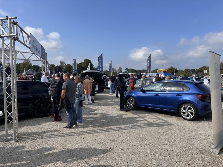 Großes Interesse an der Automobil Ausstellung Erding 2025 15 Blaue und schwarze Autos auf einem Schotterplatz bei der Automobilausstellung Erding 2025, umgeben von Besuchern unter blauem Himmel mit vereinzelten Wolken.