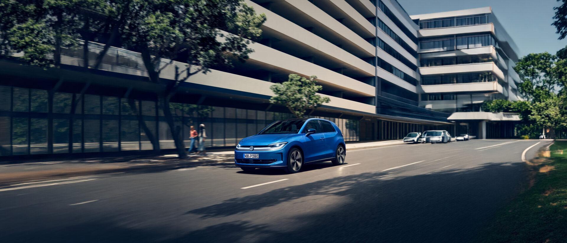 Blauer VW ID. Polo fährt auf einer Straße vor einem modernen Bürogebäude mit Glasfassade und mehreren Stockwerken.