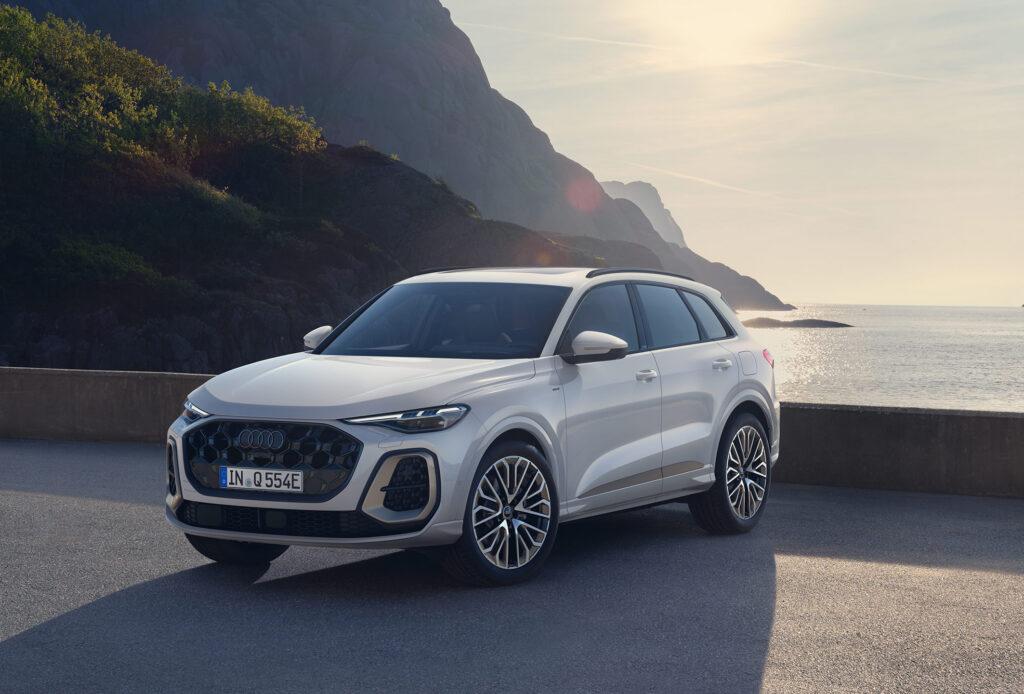 Weißer Audi SUV steht auf einer Küstenstraße mit Berglandschaft im Hintergrund bei Sonnenuntergang